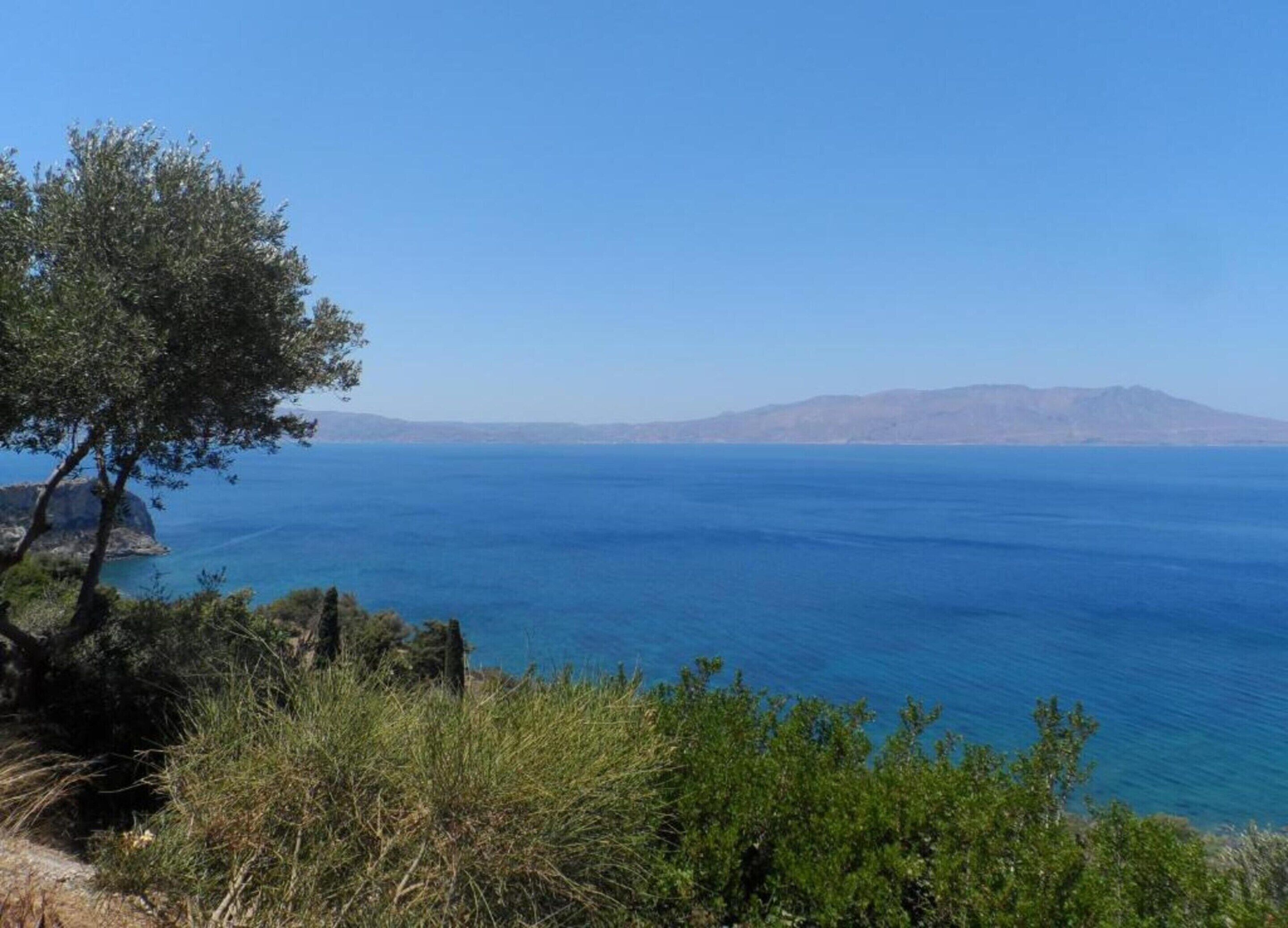 A coastal landscape with a clear view of the sea and distant mountains.