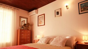 A bedroom with a wooden ceiling, a bed with white bedding, a wooden dresser, and two wall-mounted lamps. - Apartment in Croatia With Balcony (Malinska-Dubasnica)