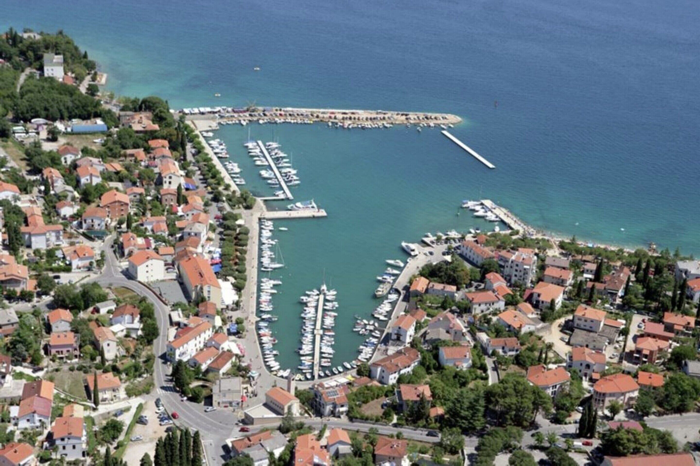 Eine Luftaufnahme einer Küstenstadt mit einem Yachthafen, Wohngebäuden und einem Steg, der ins Meer führt.