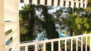 A view from a balcony with a striped ceiling, overlooking a pool area surrounded by trees. - Apartment in Croatia With Balcony (Malinska-Dubasnica)