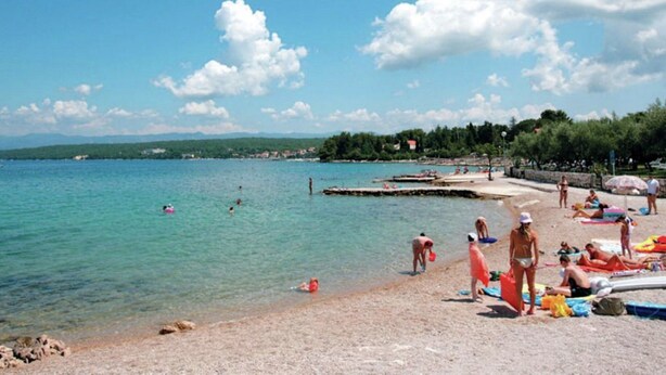 A beach with clear turquoise water, people sunbathing, and a distant shoreline with trees and buildings. - Apartment in Croatia With Balcony (Malinska-Dubasnica)