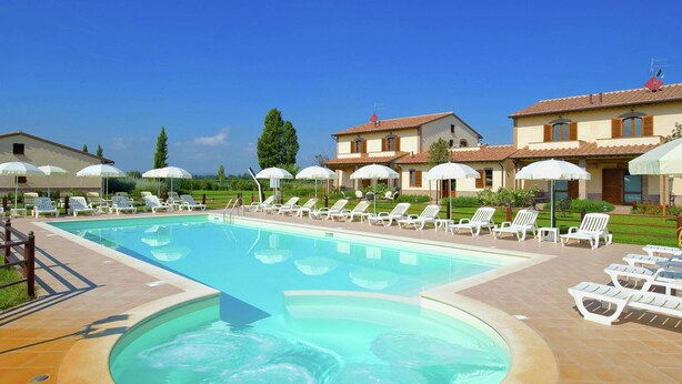 A swimming pool with sun loungers and umbrellas, surrounded by a brick patio and a building with a tiled roof.