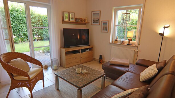 A living room with a brown leather sofa, a wicker chair, a television, and a window with a view of greenery.