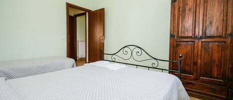 A bedroom with two beds, a wooden wardrobe, and a door leading to another room.