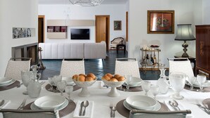 Ein Essbereich mit gedecktem Tisch, einer Couch im Hintergrund und einer modernen Deckenleuchte.