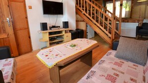 Una habitación acogedora con una escalera de madera, un televisor de pantalla plana en la pared y una pequeña mesa con mantel floreado.
