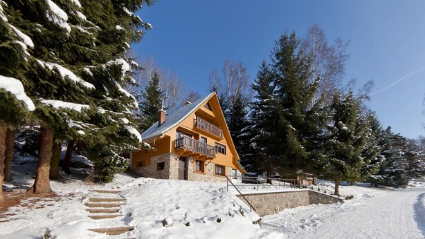 Una cabaña con base de piedra, un balcón y un paisaje cubierto de nieve.