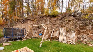 Un patio trasero con un columpio de madera, un trampolín y un arenero.
