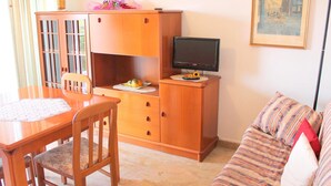 A cozy living room with a wooden cabinet, a television, a sofa, and a dining table with chairs.