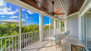 A covered balcony with a ceiling fan, a table with chairs, and a view of greenery and buildings. - Siesta Soul | Multilevel Home Located in Siesta Key Village w/ Private Pool, Fire Pit, Walk to Beach (Siesta Key)