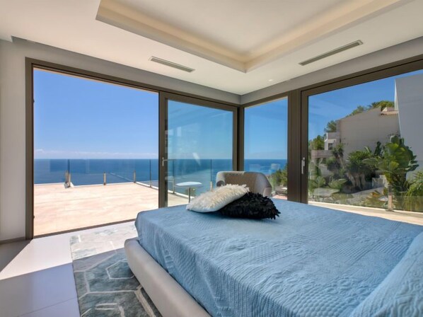 A bedroom with a large bed, a view of the sea, and a balcony with a chair.