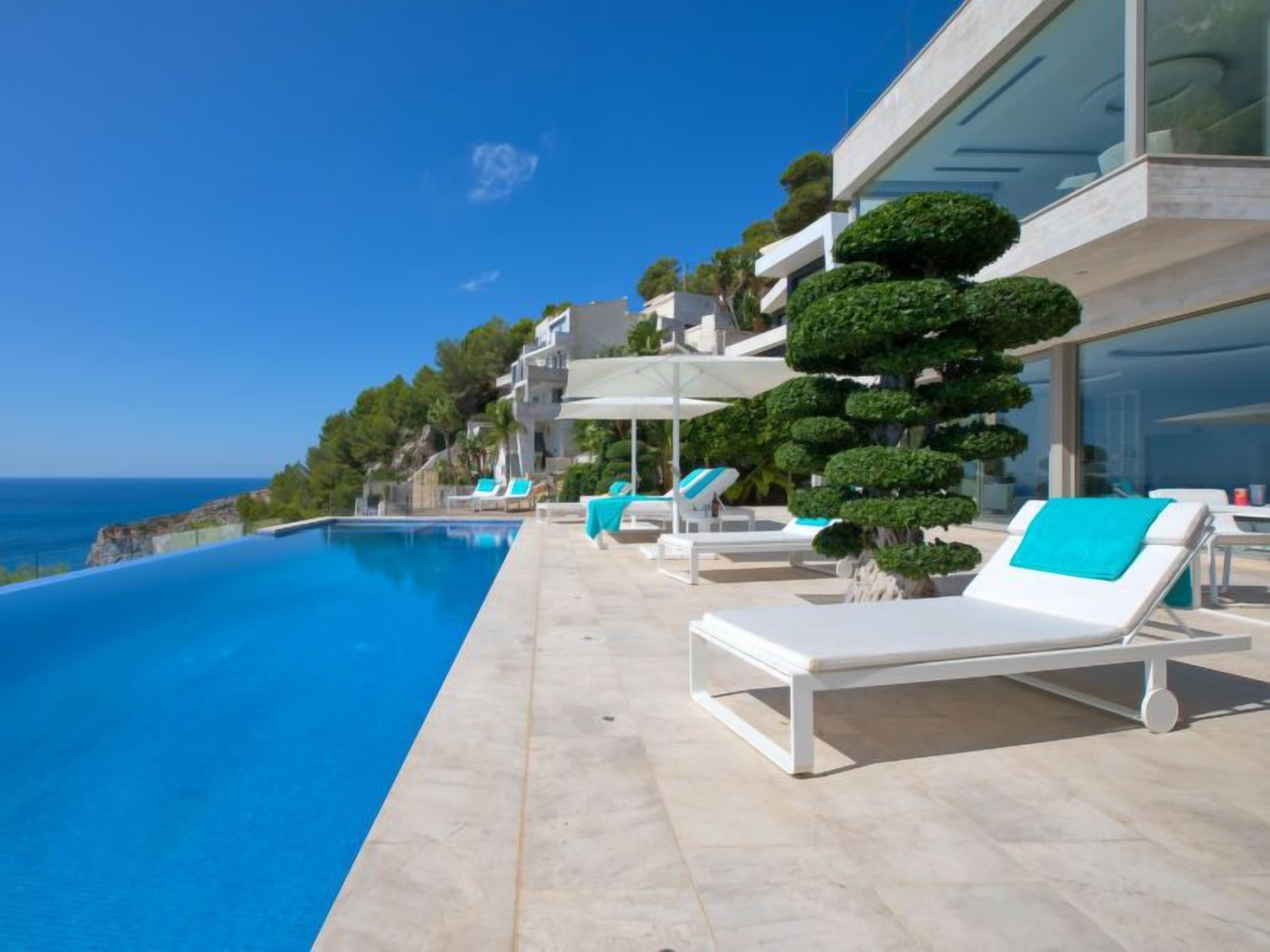 A modern resort with a pool, sun loungers, and a view of the sea.