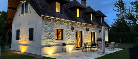 A two-story house with a stone facade, multiple windows, and a patio area with outdoor furniture.