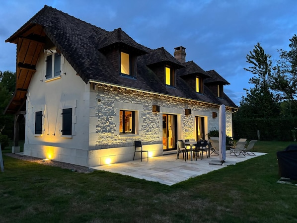 A two-story house with a stone facade, multiple windows, and a patio area with outdoor furniture.