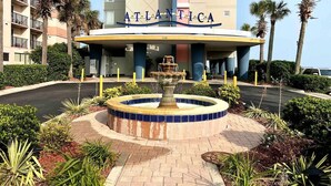 A hotel entrance with a fountain, palm trees, and a building labeled "ATLANTICA".