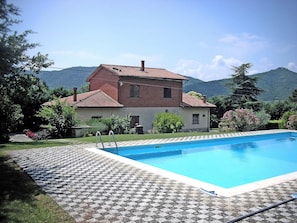 A house with a swimming pool, surrounded by a garden and mountains in the background.