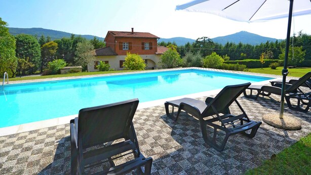A swimming pool with lounge chairs and an umbrella, surrounded by a house and mountains. - Belvilla by OYO Villa Mimosa (Cortona)