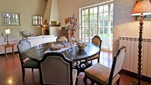 A dining area with a round table, chairs, and a fireplace. There is a window with a view of greenery outside. - Belvilla by OYO Villa Mimosa (Cortona)