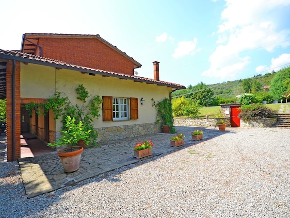 A rustic house with a stone foundation, a tiled roof, and a gravel driveway.