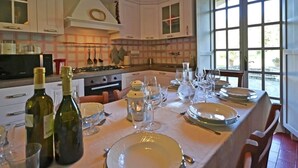 A well-lit kitchen with white cabinets, a dining table set for six with wine bottles, glasses, and plates. - Belvilla by OYO Villa Mimosa (Cortona)