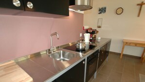 A kitchen with a stainless steel sink, a stove, and a small wooden table. - Apartment in Blatten With Mountain Views & Open Kitchen (Blatten)