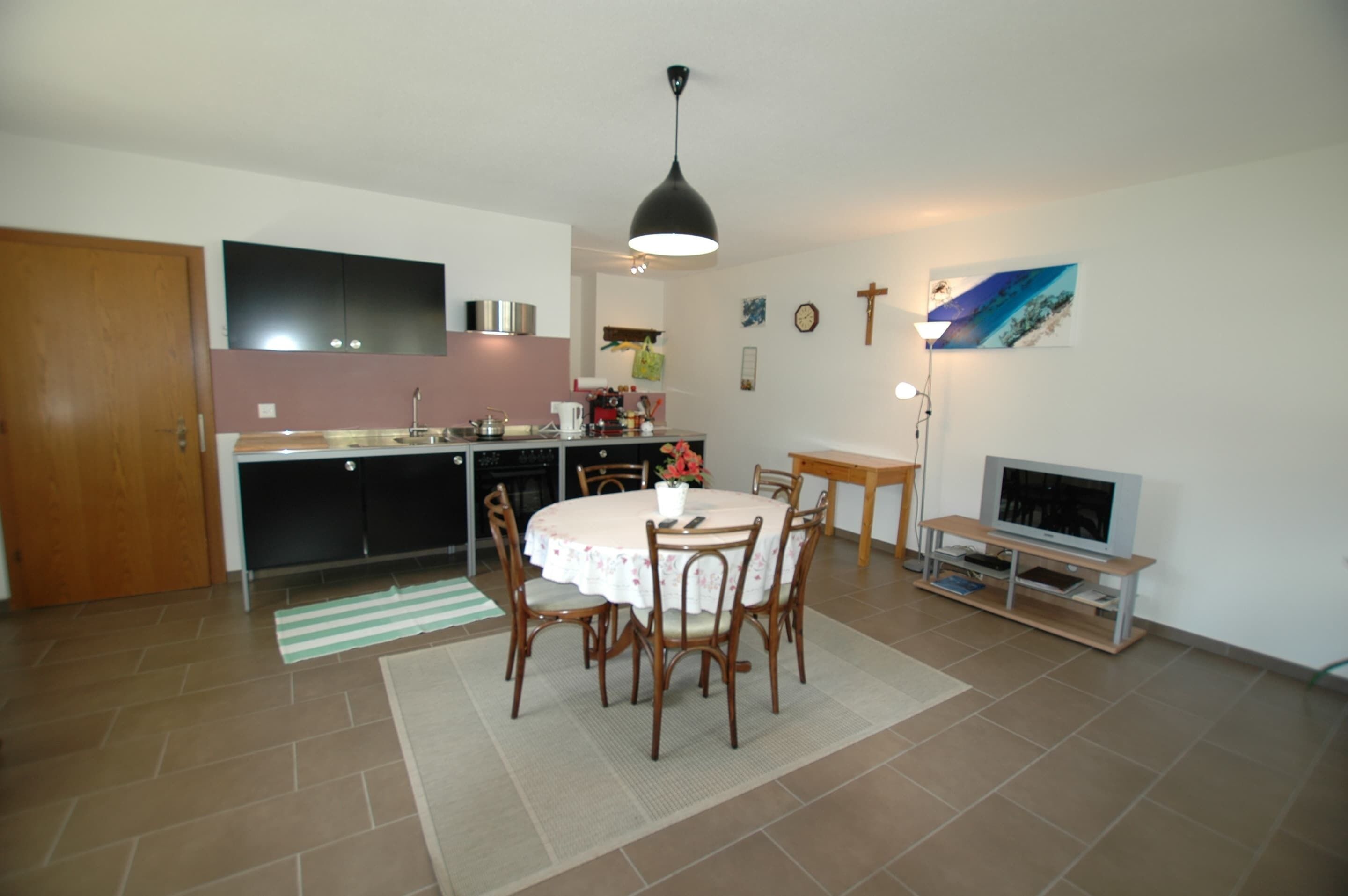 A kitchen with a dining table, chairs, a TV, and a cross on the wall.