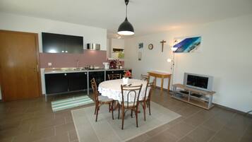 A kitchen with a dining table, chairs, a TV, and a cross on the wall.