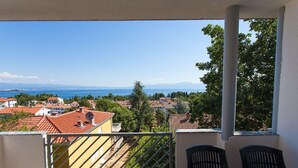 A balcony with a view of a coastal town, a table, and two chairs. - Apartment With Terrace, Sea View, Pool & Outdoor Kitchen (Malinska-Dubasnica)