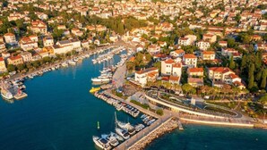 An aerial view of a coastal town with a marina, residential buildings, and a curved road. - Apartment With Terrace, Sea View, Pool & Outdoor Kitchen (Malinska-Dubasnica)
