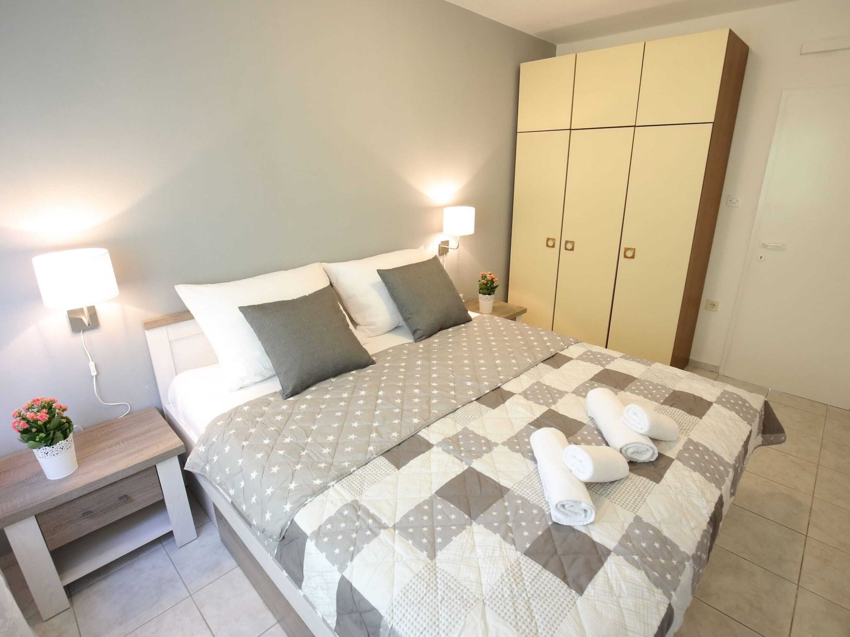 A neatly made bed with a quilt, two bedside tables with lamps, a wooden nightstand, and a wardrobe.