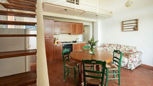 Een eetruimte met een ronde tafel en vier stoelen, een keuken met houten kastjes, en een balkon met een leuning.