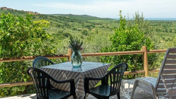 Een terras met een tafel en stoelen, met uitzicht op een weelderig landschap met heuvels en groen.