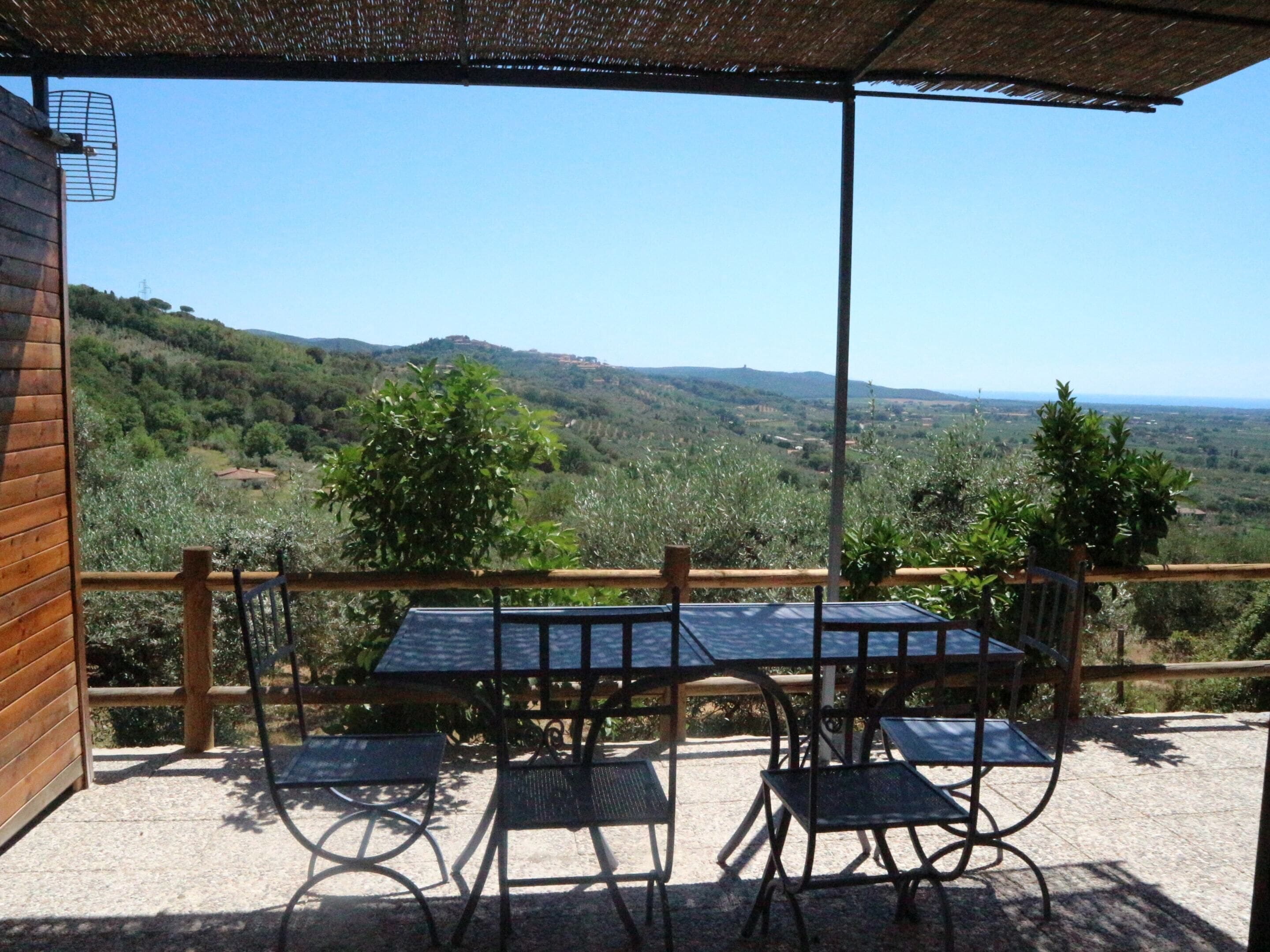 An outdoor patio with a table and chairs, overlooking a hilly landscape.