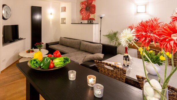 A modern living room with a sofa, a dining table with a salad, candles, and a large flower arrangement.
