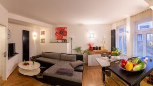 A modern living room with a grey sofa, a round coffee table, and a dining table with a fruit bowl.