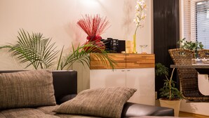 A modern living room with a sofa, a coffee table, and a dining area with wicker chairs.