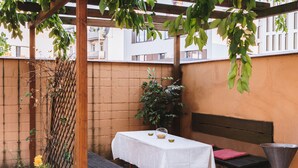 An outdoor patio with a table covered in a white tablecloth, a bench, and a metal container.