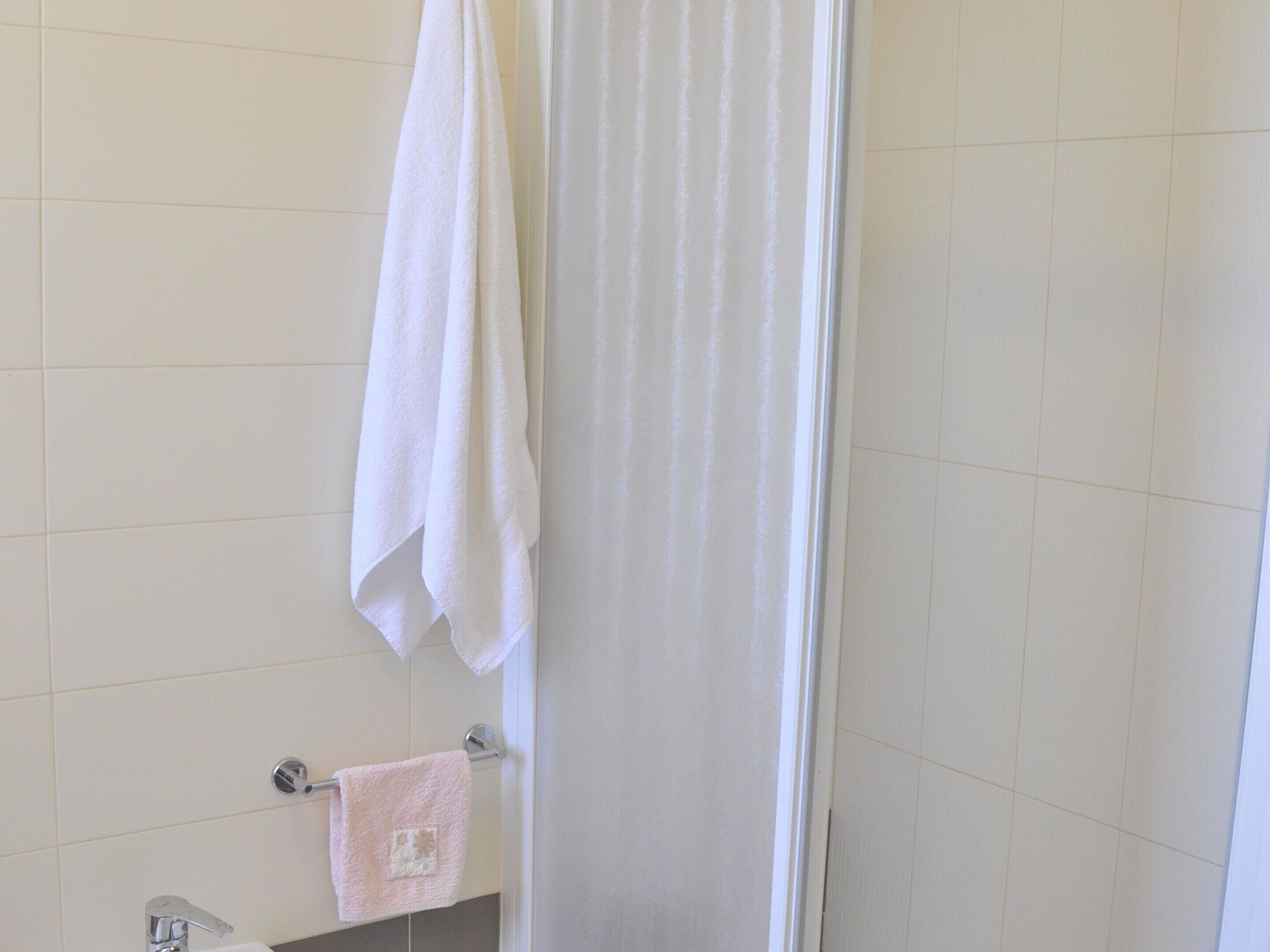 Une salle de bain avec des carreaux blancs, un rideau de douche et deux serviettes suspendues à un porte-serviettes.