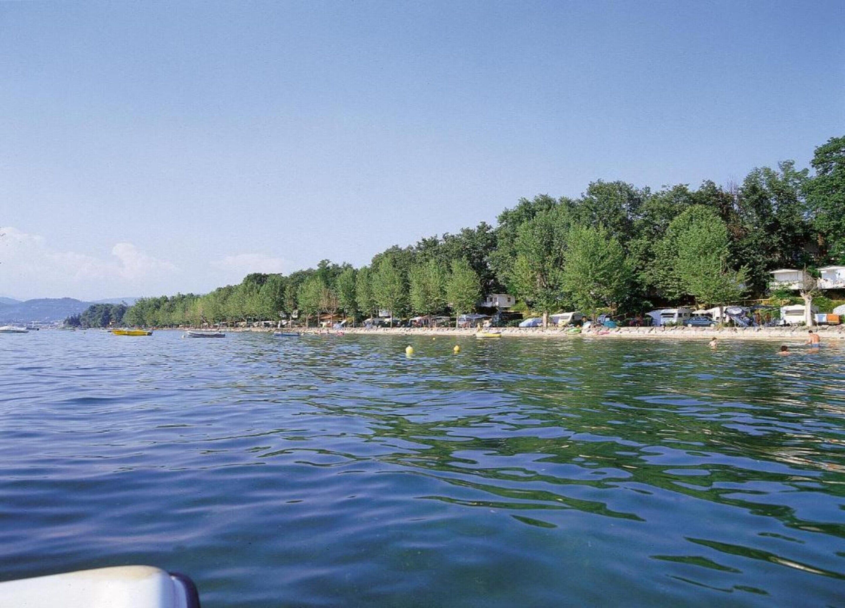 Vista de un lago con barcos, una playa de arena y una hilera de casas a lo largo de la orilla.