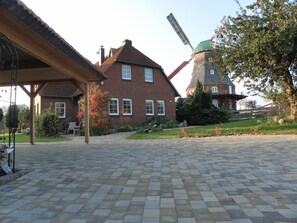 A brick house with a windmill, a covered patio, and a paved walkway. - Lovely Apartment in Neubukow near Sea (Neubukow)