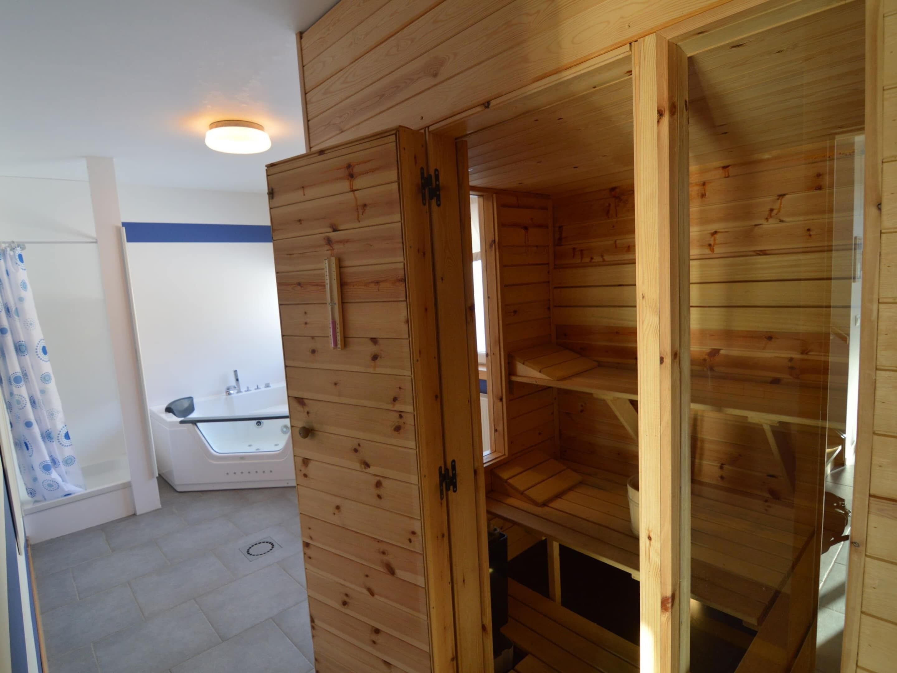 Interior de una cabaña de madera con sauna, un baño pequeño con lavamanos y cortina de ducha.