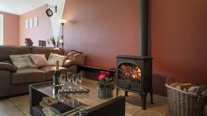 A cozy living room with a sofa, a glass-top coffee table, a fireplace, and a wicker basket. - Cushy Holiday Home With Fenced Garden (Tenneville)