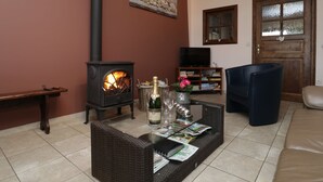 A living room with a fireplace, a sofa, a coffee table with magazines, a television, and a bookshelf. - Cushy Holiday Home With Fenced Garden (Tenneville)