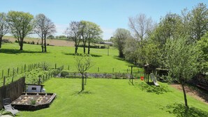 A grassy outdoor area with trees, a wooden bench, and a small shed. - Cushy Holiday Home With Fenced Garden (Tenneville)