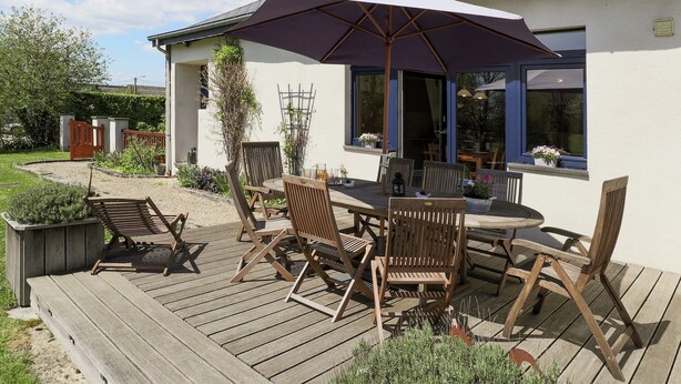 A wooden deck with outdoor furniture, a covered patio area, and a house with a white exterior and blue trim. - Cushy Holiday Home With Fenced Garden (Tenneville)