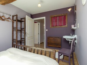 A bedroom with a bed, a wooden chair, a desk, a wardrobe, a mirror, and a bathroom with a sink and a toilet. - Cushy Holiday Home With Fenced Garden (Tenneville)