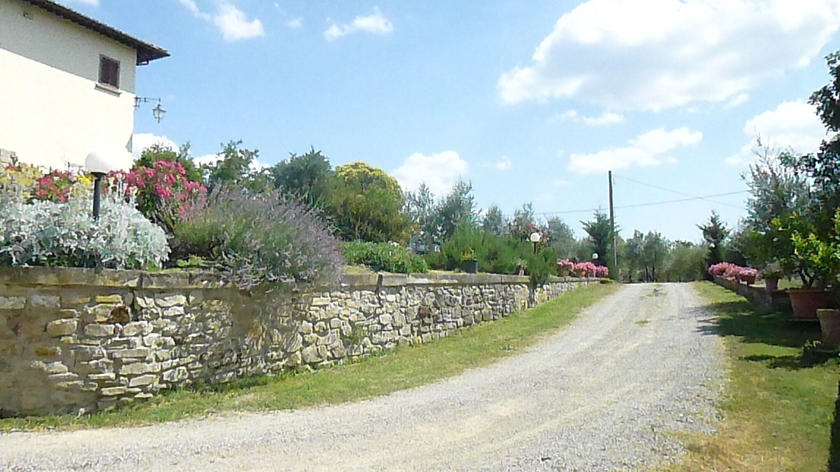 A rural road with a stone wall on one side and a building with a white facade.