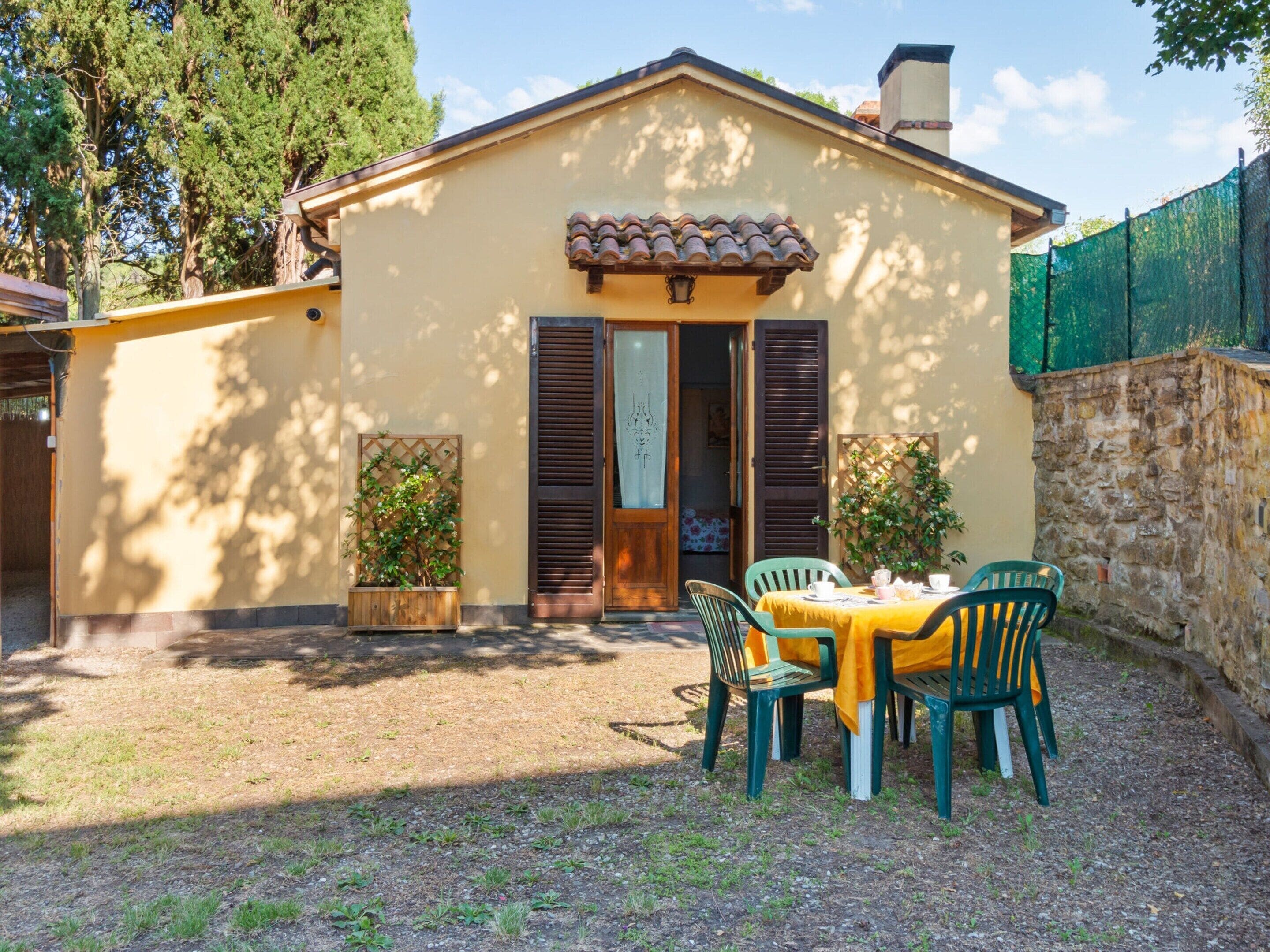 A small house with a tiled roof, wooden shutters, and a table with chairs outside.