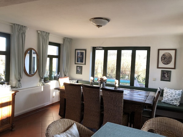 Ein Essbereich mit Korbmöbeln, einem Tisch, Stühlen, einem Fenster mit Vorhängen und gerahmten Bildern an der Wand.