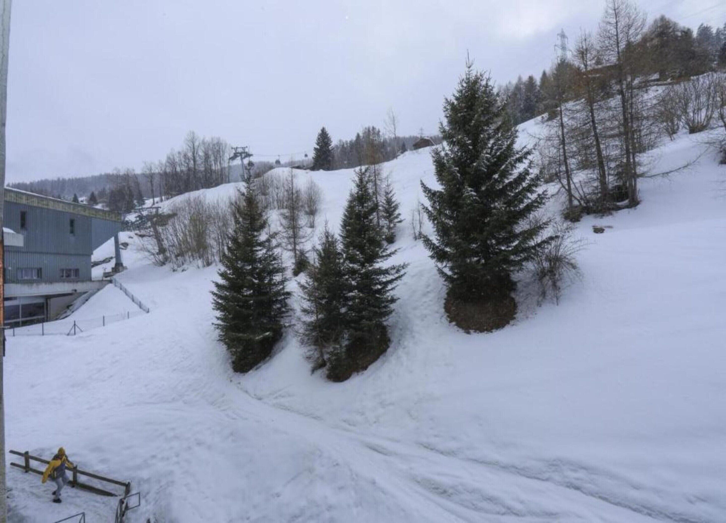 A snowy landscape with a ski lift, trees, and a building.